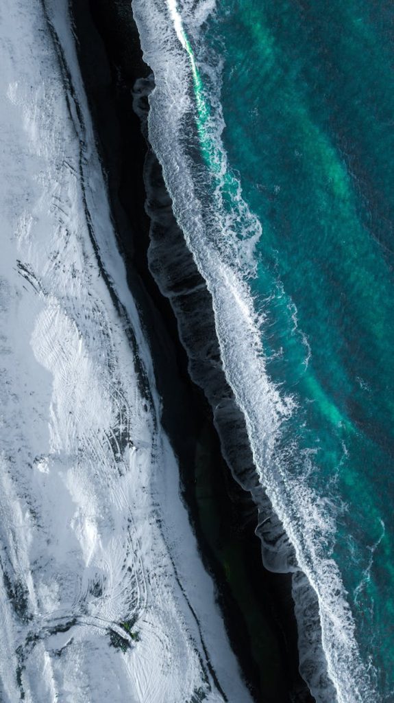 Dramatic aerial view of a snowy coastline meeting the turquoise sea in Sakhalin, Russia.